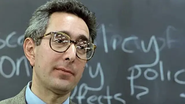 a man wearing glasses standing in front of a chalkboard