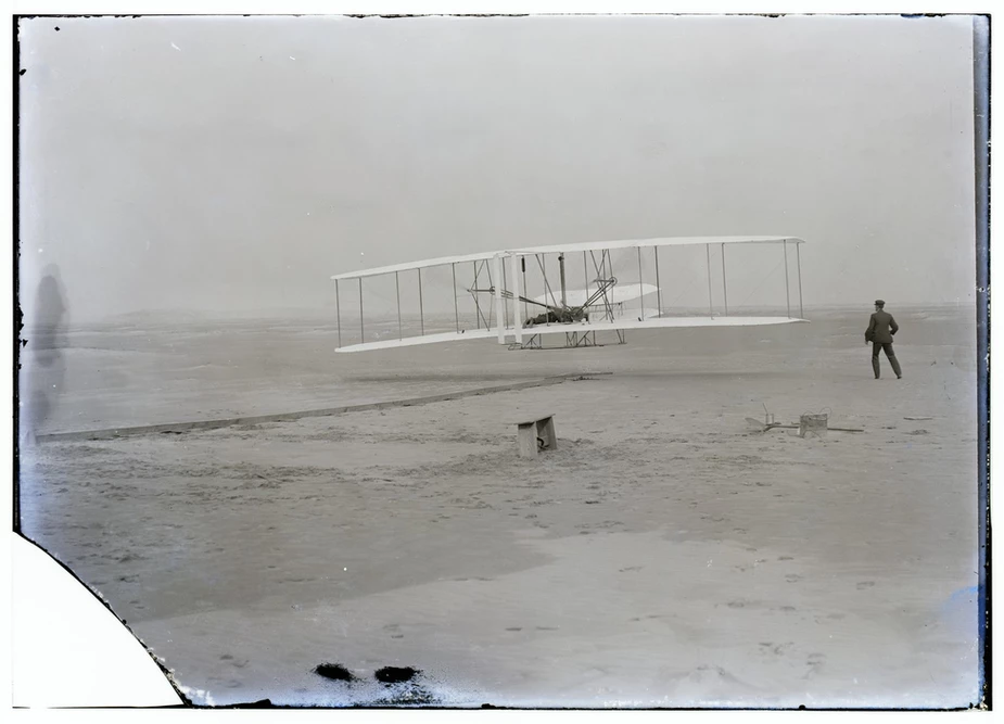 an old photo of a man standing next to a plane