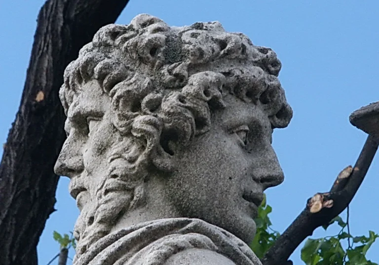 a stone statue holding an umbrella next to a tree