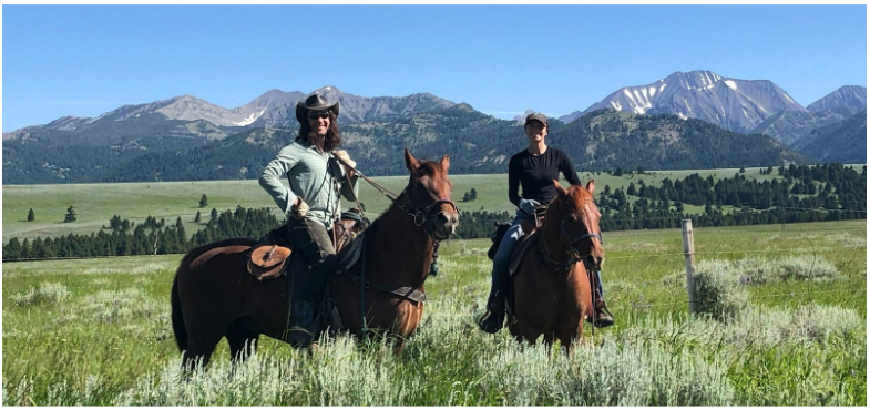 two people riding horses in a field with mountains in the background