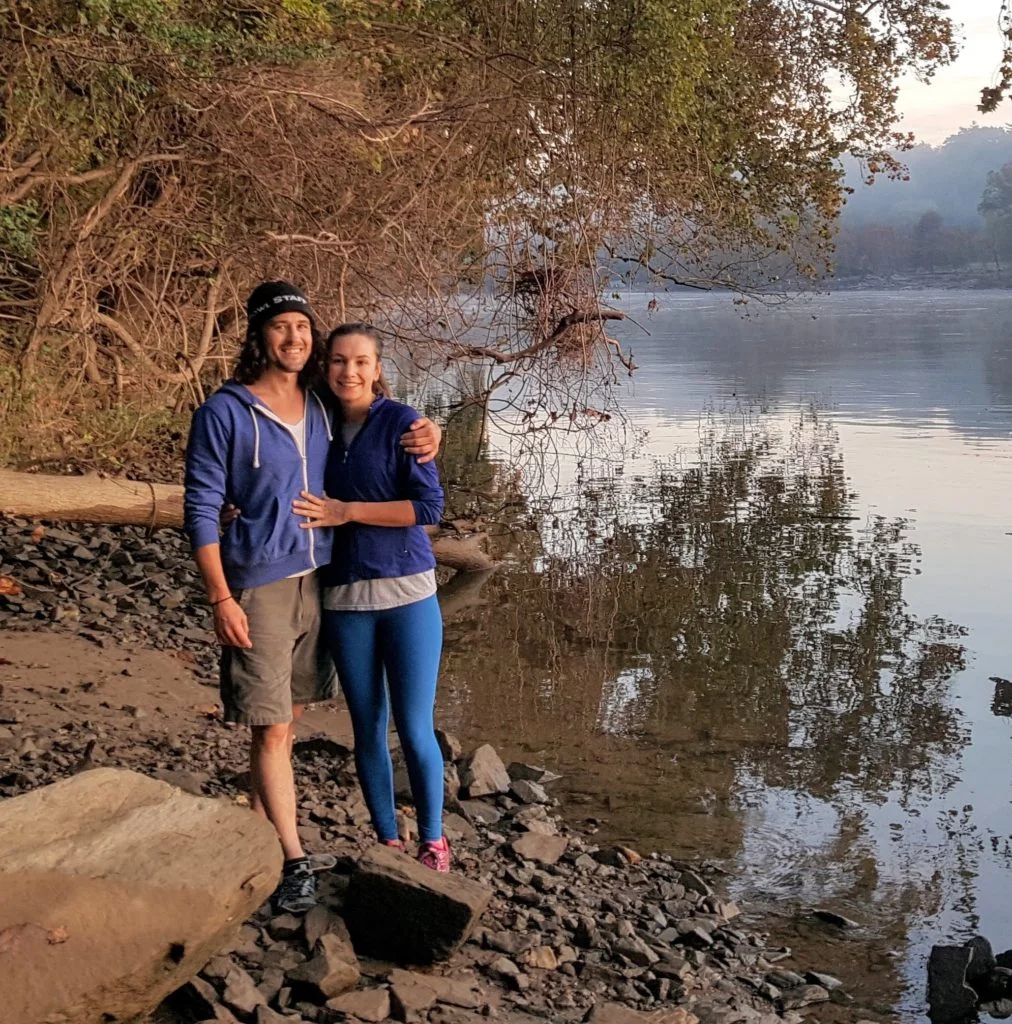 two people standing next to each other near water