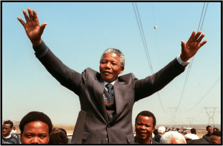 a man in a suit and tie standing with his hands up