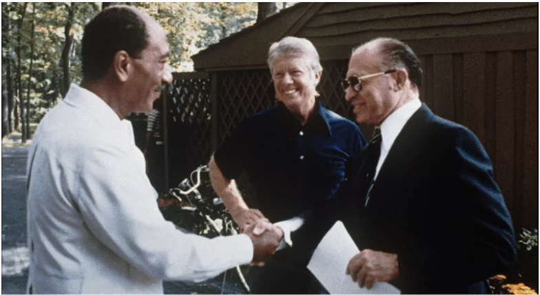 three men shaking hands in front of a fence