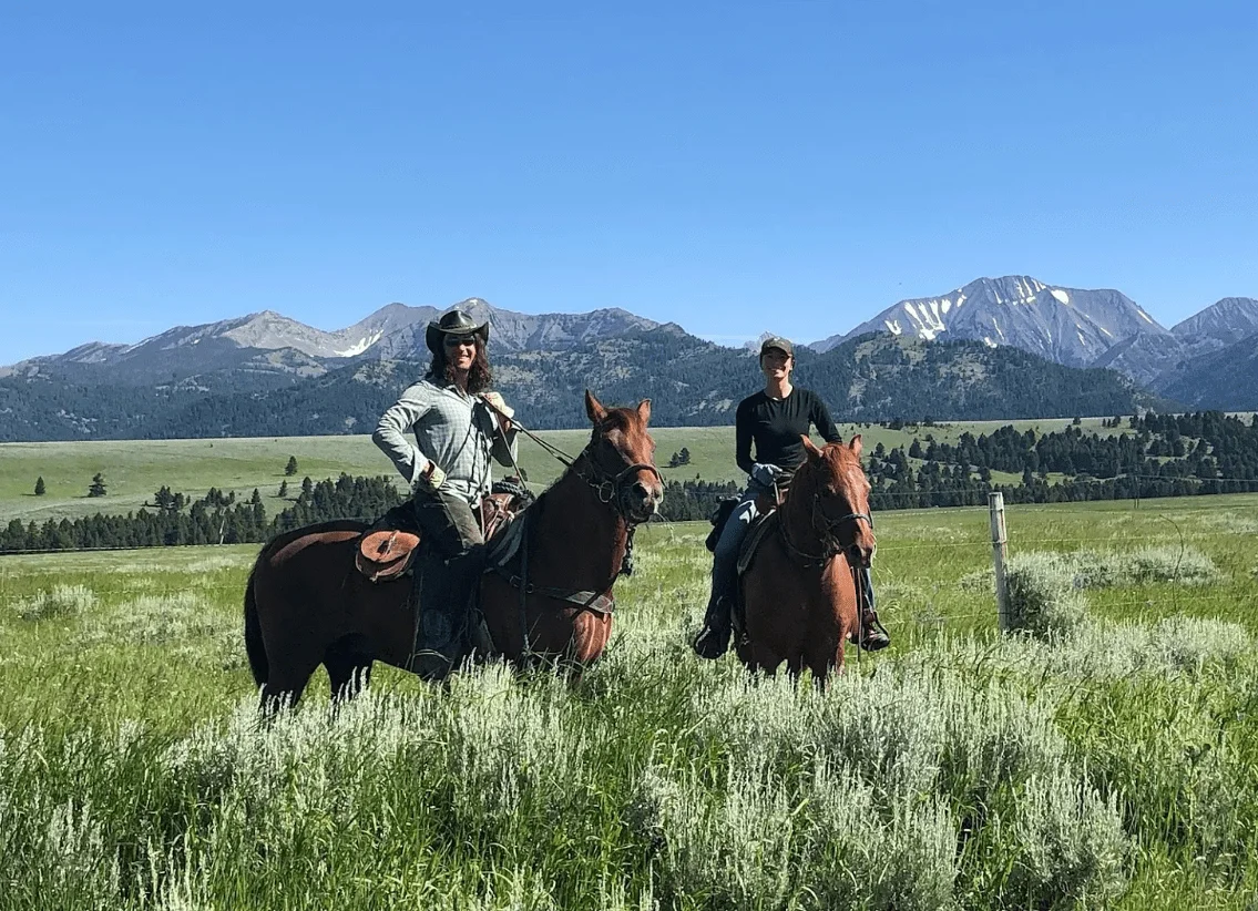 Screenshot 2024-01-05 124251 two people riding horses in a field with mountains in the background